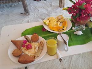 a table with two plates of breakfast food and orange juice at Mudi House in Jambiani