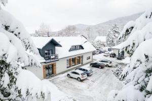a house with cars parked in a parking lot covered in snow at Apartamenty Szaron 250 m do kortów tenisowych i Bulwarów Wiślanych - Dream Apart in Ustroń