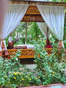 eine Bank mit Vorhängen und Blumen im Garten in der Unterkunft Hotel Asia Bukhara in Buxoro