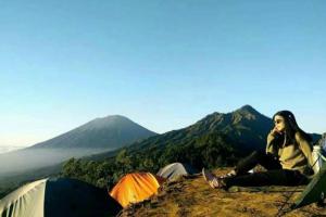 Baturaja的住宿－Batur Sunset Sunrise camping，坐在山顶的有帐篷的女人