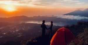 Baturaja的住宿－Batur Sunset Sunrise camping，一对夫妇站在山顶上,靠在帐篷旁边