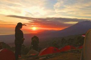 Baturaja的住宿－Batur Sunset Sunrise camping，站在山顶上望着日落的人