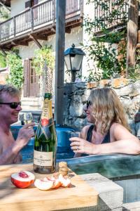 a man and woman sitting at a table with a bottle of wine at Luxury Chalet with outdoor Hot Tub, Sauna, Gardens & Mountain Views! in Briançon