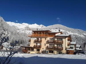 un grande edificio nella neve con montagne sullo sfondo di Hotel Ortles Dolomiti Walking & Spa a Cogolo