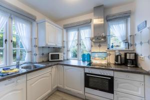 a kitchen with white cabinets and a sink and windows at Dat Südstrandhuus- Ferienwohnung Silke in Wyk auf Föhr