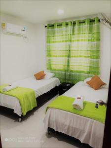 Habitación con 2 camas con sábanas verdes y ventana en Hotel Don Jose en Ciénaga
