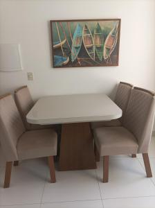 una mesa blanca y dos sillas con una pintura de barcos en Seu apartamento em Ilhéus, en Ilhéus