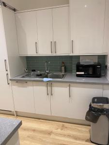 kuchnia z białymi szafkami, zlewem i kuchenką mikrofalową w obiekcie I&J Suites w mieście Woolwich