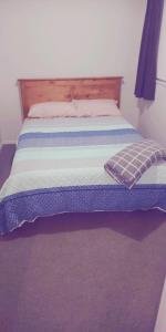 a bed with a blue and white blanket on it at Modest comfortable relaxed home away from home in Rotorua