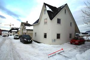 a white house with a black roof in the snow at Sentral leilighet med 3 soverom in Harstad