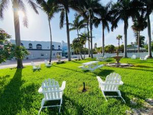 zwei weiße Stühle im Gras mit Palmen in der Unterkunft La Tortuga Historic Pass A Grille St Pete Beach 1 in St Pete Beach