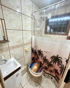 a bathroom with a toilet with a palm tree shower curtain at Pousada Happy in São Francisco do Sul