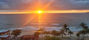 a sunset on the beach with the sun setting over the ocean at Apartamento Ubatuba Reserva DNA in Ubatuba