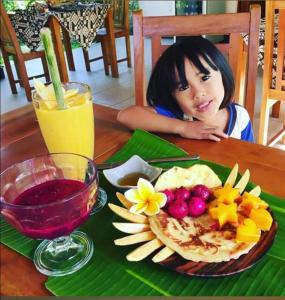 una niña sentada en una mesa con un plato de comida en Mango Moon, en Pemuteran
