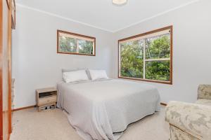 een witte slaapkamer met een bed en een raam bij Surfers Lookout - Waipu Cove Holiday Home in Waipu