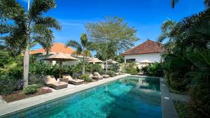 a swimming pool with chairs and umbrellas next to a house at Green Valley Lombok in Selong Belanak