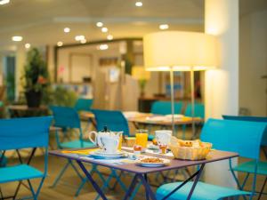 a table with food and drinks and blue chairs at Résidence Vacances Bleues Les Jardins d'Arvor in Bénodet