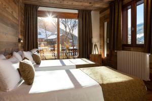 two beds in a room with a large window at Hôtel et Spa Le Vermont in Le Grand-Bornand