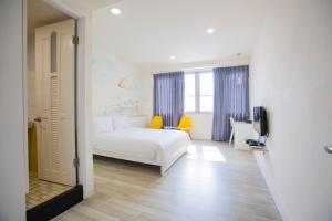 a bedroom with a white bed and a yellow chair at Key We Go Hotel 奇遇果人文旅店 in Tainan