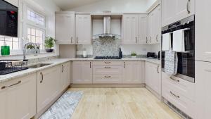 a white kitchen with white cabinets and a wooden floor at JDB Romford 5-Bedroom House with parking in Goodmayes