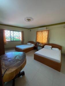 1 dormitorio con 2 camas, mesa y ventanas en Apsara Guest House Kampot City, en Kampot