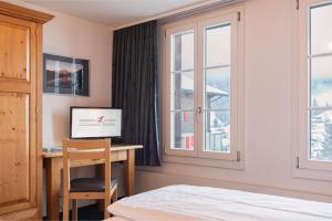 a bedroom with a desk and a bed and windows at Jungfrau Lodge, Swiss Mountain Hotel in Grindelwald