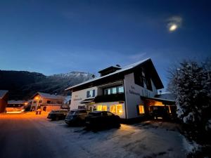 ein Haus mit Autos, die nachts im Schnee geparkt sind in der Unterkunft Hotel-Garni Kalkbrennerhof in Pfronten