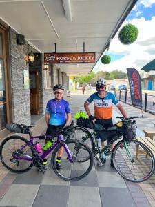 dos hombres parados con sus bicicletas delante de una tienda en Horse and Jockey Inn, en Matamata