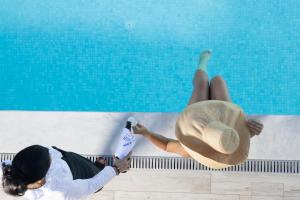 a woman in a hat sitting next to a swimming pool at White Pearl in Pefkochori