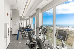 un gimnasio con cintas de correr, máquinas elípticas y ventanas en Lighthouse 714, en Gulf Shores