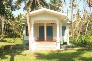 a small white house with a porch with palm trees at The Temple Tree Varkala in Varkala