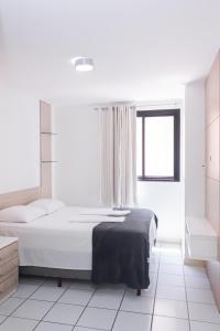 ein weißes Schlafzimmer mit einem Bett und einem Fenster in der Unterkunft Apartamento Aconchegante na Orla de Pajuçara in Maceió