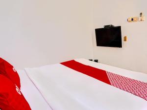 1 cama roja y blanca con TV en la pared en OYO Life 92021 Dua Putra Homestay Klayar, en Watukarung