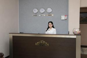 una mujer de pie detrás de una recepción con relojes en la pared en Classic Hotel, en Qusar