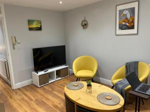 sala de estar con mesa, sillas amarillas y TV en 2 Bedroom Apartment Chiswick Park Tube Station, en Londres
