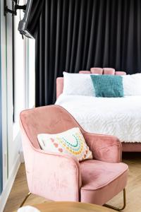 a pink chair with a pillow and a bed at Le Virtuose - Vieux-Terrebonne in Terrebonne