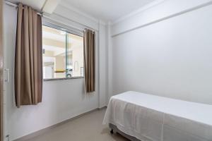 een witte slaapkamer met een bed en een spiegel bij Apto Pertinho da Avenida da Praia de Bombas - 2 dorms 4 pessoas in Bombinhas
