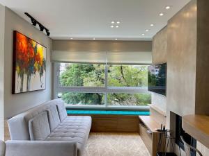 una sala de estar con sofá y una piscina a través de una ventana en Apartamentos Residencial Villa Rossa by Achei Gramado, en Gramado