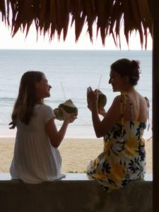 Dos mujeres sentadas en la playa bebiendo. en Sealord Naithon Beachfront Villa en Nai Thon Beach