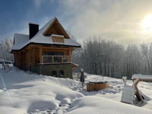 Una cabaña de madera cubierta de nieve con el sol detrás. en Cinalkowa 6, na Górze Żar en Międzybrodzie Żywieckie