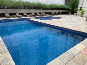 a swimming pool with blue water and chairs at Flat Jardins, entre Av Paulista e Parque do Ibiraquera in Sao Paulo