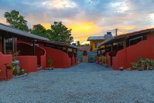 un camino entre dos edificios rojos con una puesta de sol en el fondo en Kalug - Chalé Chão de Trancoso Studios, en Trancoso