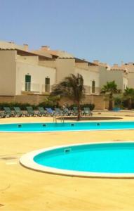 zwei Swimmingpools mit Stühlen, Palmen und Gebäuden in der Unterkunft vila verde twonhouse T54 in Santa Maria