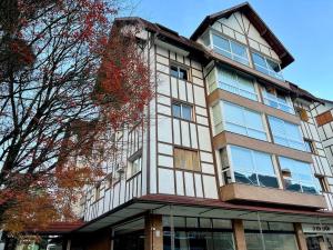 ein hohes weißes Gebäude mit Fenstern und einem Baum in der Unterkunft Apartamentos Gartenberg no CENTRO by Achei Gramado in Gramado