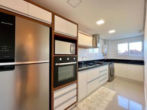 una cocina con electrodomésticos de acero inoxidable y armarios blancos en Apartamentos Gartenberg no CENTRO by Achei Gramado, en Gramado
