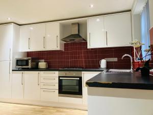 uma cozinha com armários brancos e uma parede de azulejos vermelhos em Cosy home near hospital em Carlisle
