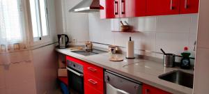 a small kitchen with red cabinets and a sink at Apartamento TomCar Piscina, Pádel, wifi y zonas comunes in Sanlúcar de Barrameda