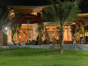 a palm tree with an umbrella in front of a building at TROPICAL HOUSE RIVERSIDE RETREAT in Thuan An