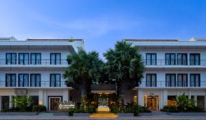 a white building with palm trees in front of it at Koulen Hotel in Siem Reap