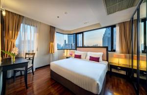 a hotel room with a bed and a desk and windows at Bandara Silom Suites, Bangkok in Bangkok
